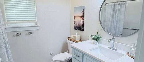 A bathroom with a toilet, sink, mirror, and a window with blinds.