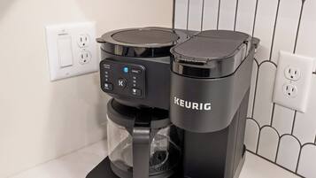 Una cafetera Keurig sobre una encimera con salpicadero blanco de azulejos y armarios de madera arriba.