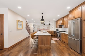A modern kitchen with wooden cabinets, a stainless steel refrigerator, and a central island with bar stools.