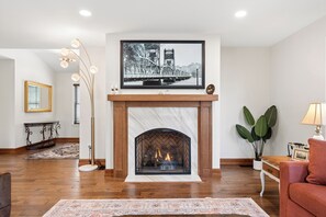 A living room with a fireplace, a large framed picture above it, a floor lamp, and a potted plant.