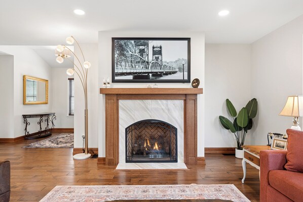A living room with a fireplace, a large framed picture above it, a floor lamp, and a potted plant.
