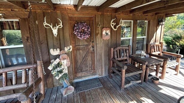 A rustic wooden cabin with a wooden porch, a door with antlers, a wreath, and a sign reading 'Sutton Cabin.' - Cozy 1-bedroom cabin in perfect Wathena with AC (Wathena)