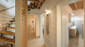 Ein modernes Interieur mit einer Holztreppe und einem Flur, der zu einem Badezimmer mit Waschbecken und Spiegel führt.