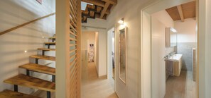 Ein modernes Interieur mit einer Holztreppe und einem Flur, der zu einem Badezimmer mit Waschbecken und Spiegel führt.