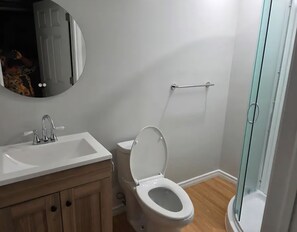 Un baño con lavamanos blanco, inodoro y cabina de ducha con mampara de vidrio.