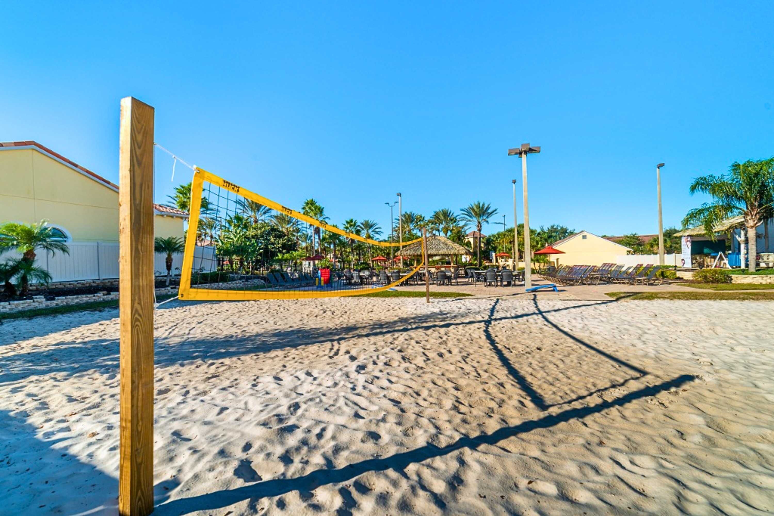 Un terrain de beach-volley avec un filet, des palmiers et un bâtiment en arrière-plan.