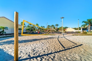 Un terrain de beach-volley avec un filet, des palmiers et un bĂątiment en arriĂšre-plan.