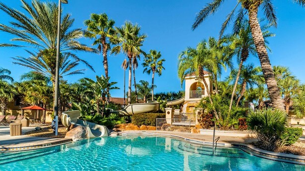 A swimming pool with palm trees, a water slide, and a building with an arched entrance. - Spacious Townhome Near Disney, Free Parking (Davenport)