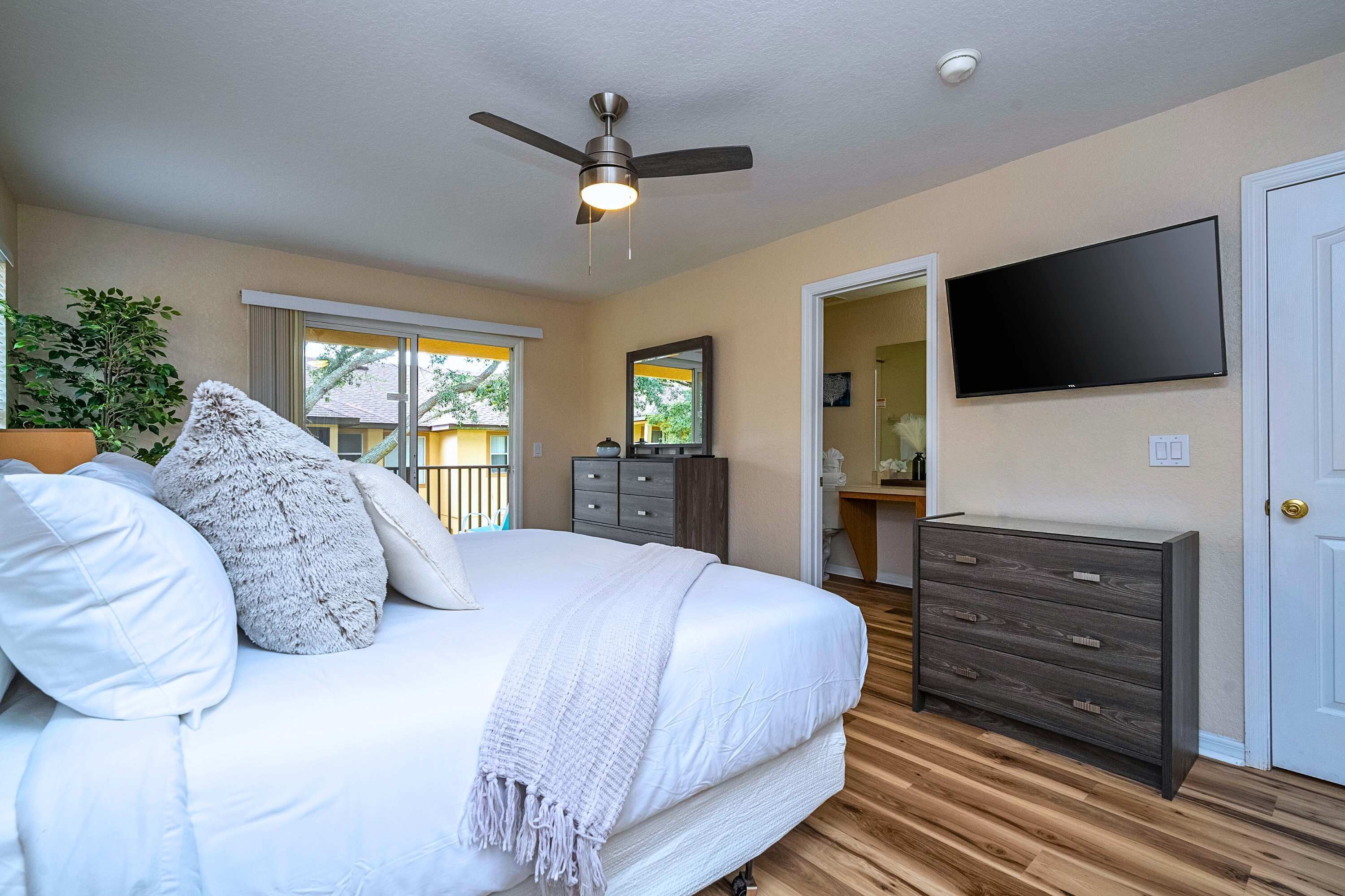 A bedroom with a bed, a ceiling fan, a dresser, a TV, and a window.