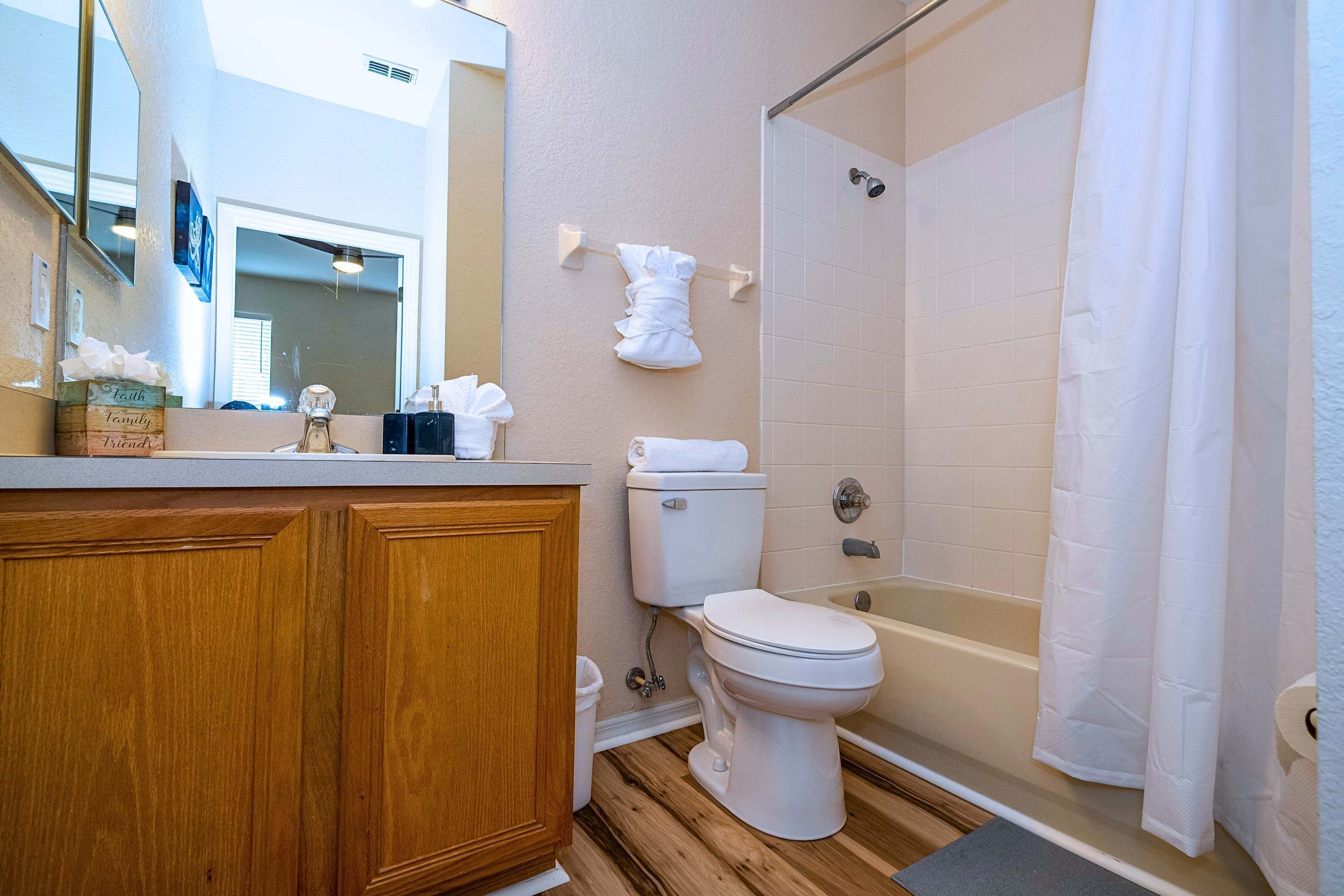 A bathroom with a wooden vanity, a toilet, a bathtub, and a shower curtain.