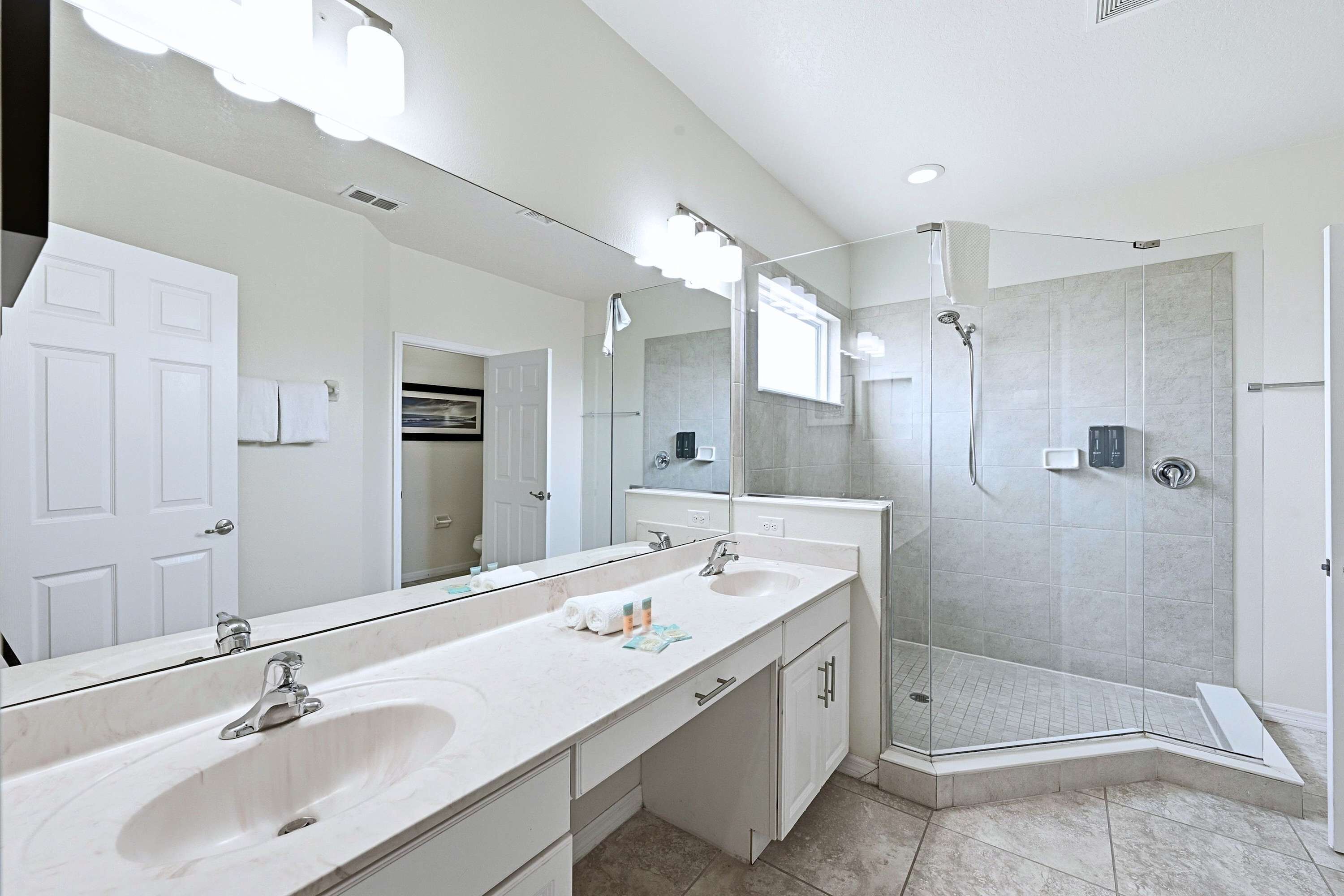Un baño moderno con un espejo grande, dos lavamanos, una ducha y un vestidor de ducha.