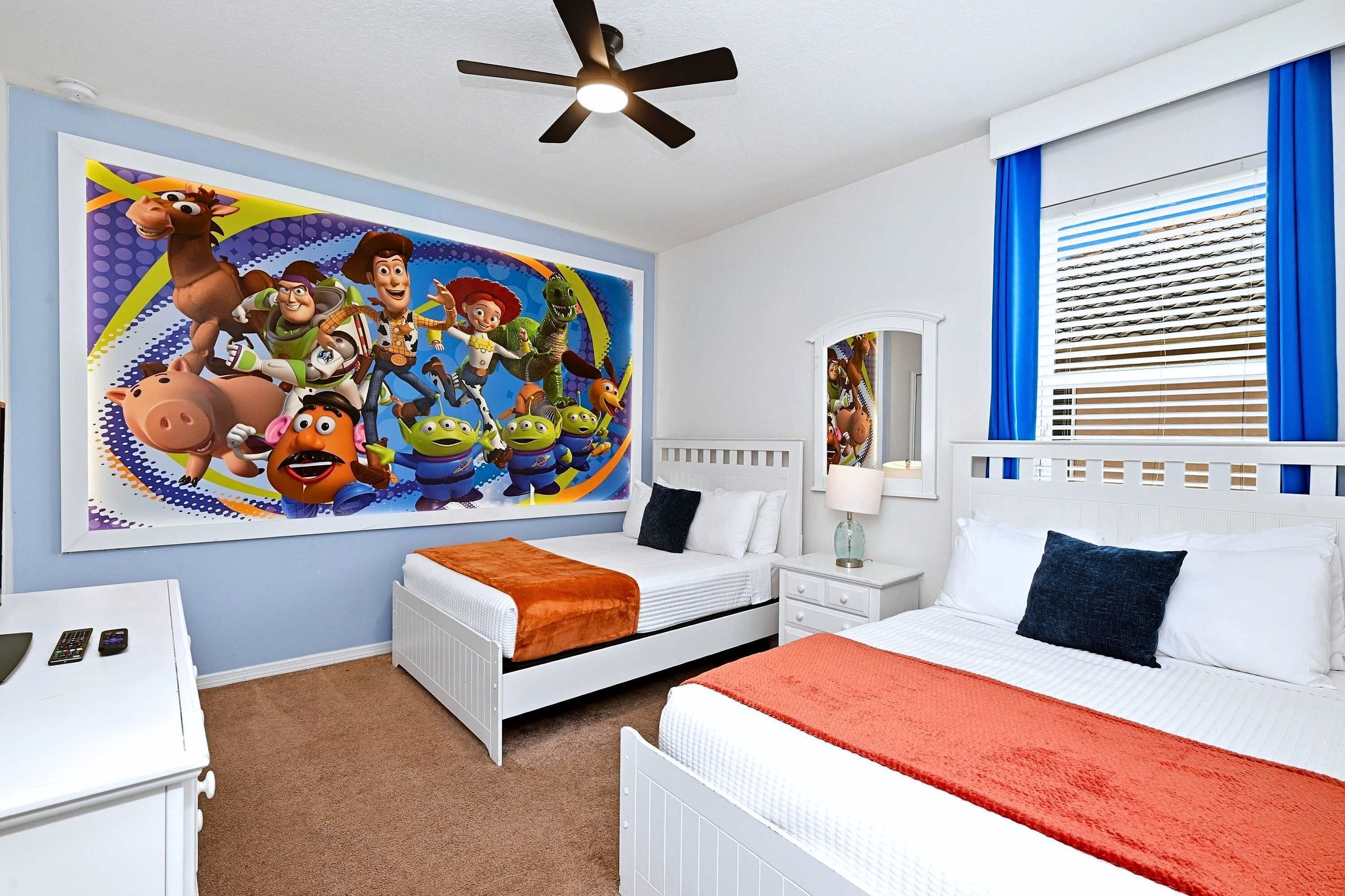 A bedroom with a bed, a nightstand, a desk, a chair, a ceiling fan, a window with blinds, and a wall mural.
