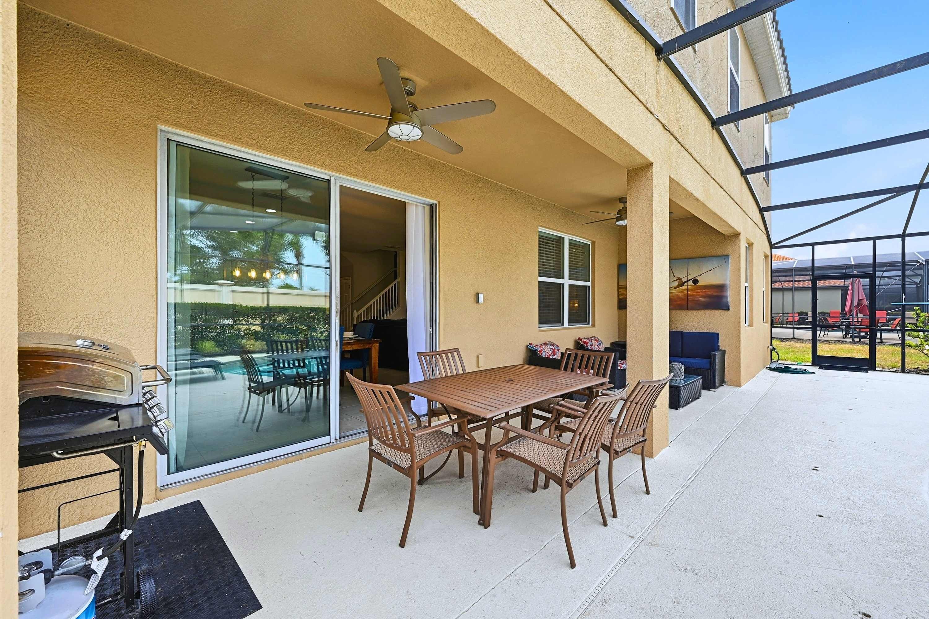 Um pátio externo com mesa e cadeiras, um ventilador de teto e uma churrasqueira.