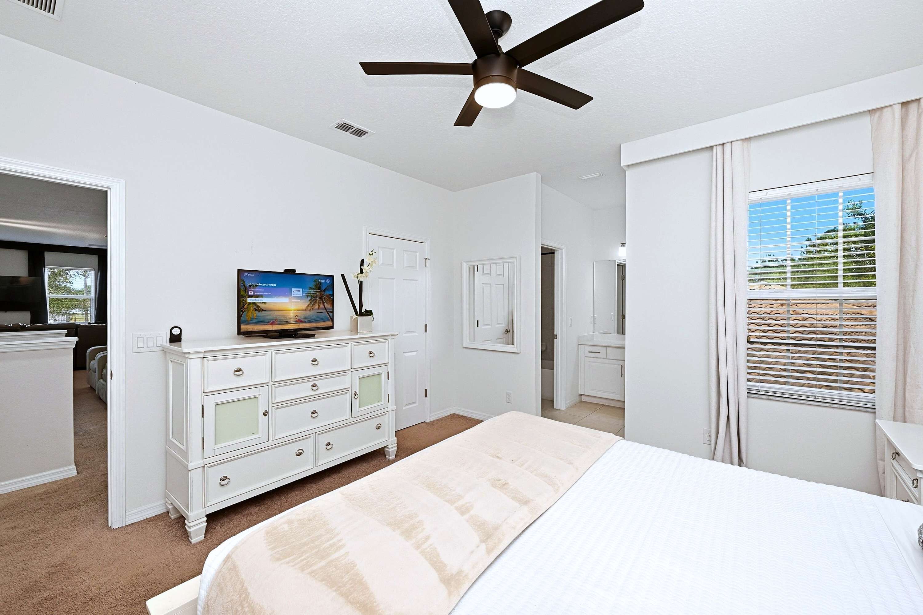 A bedroom with a bed, a dresser, a television, and a ceiling fan.