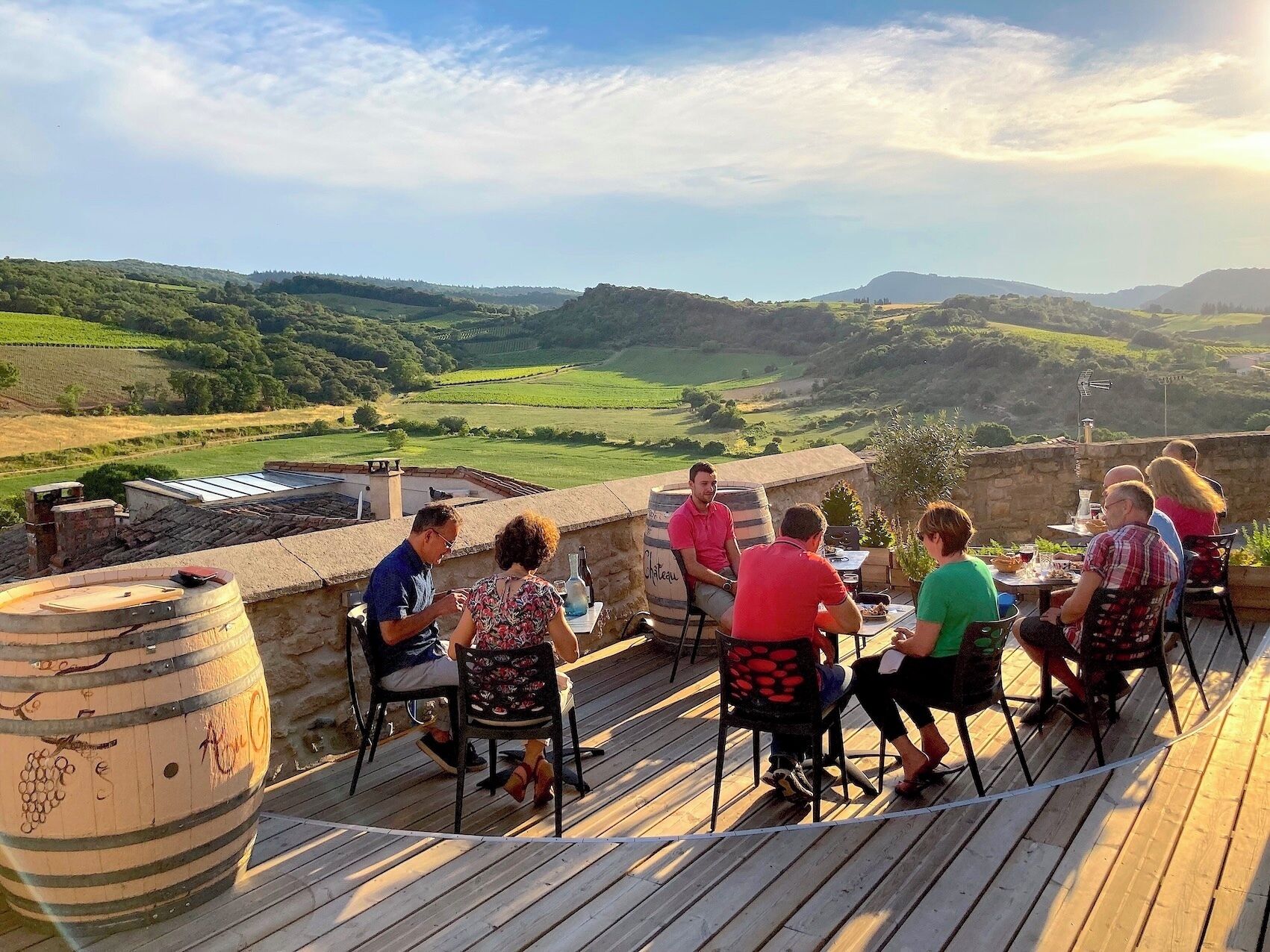 Un grupo de personas cenando al aire libre con vistas panorámicas a colinas ondulantes y viñedos.