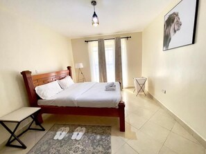 Ein Schlafzimmer mit einem Bett, einem kleinen Tisch, einem Paar Hausschuhen, einer Lampe und einem gerahmten Bild an der Wand.