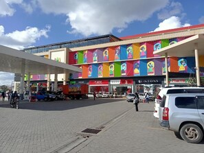 Ein Gewerbegebäude mit farbenfrohen Wandgemälden, einer Tankstelle und verschiedenen Geschäften, darunter eine Apotheke und eine Bank.