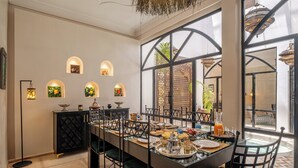 A dining area with a long table, chairs, and a black cabinet with decorative items. - Expérience Riad privé Médina Jacuzzi (Marrakech)