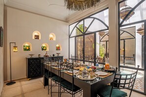 A dining area with a long table, chairs, and a black cabinet with decorative items.