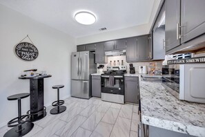 A modern kitchen with grey cabinets, a stainless steel refrigerator, a built-in oven, and a marble countertop. - 2 Kings, Family, Backyard, 15 mins to Fort Benning (Columbus)