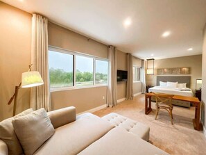 Ein Hotelzimmer mit Sofa, Bett, Fernseher, Schreibtisch und einem Fenster mit Vorhängen.
