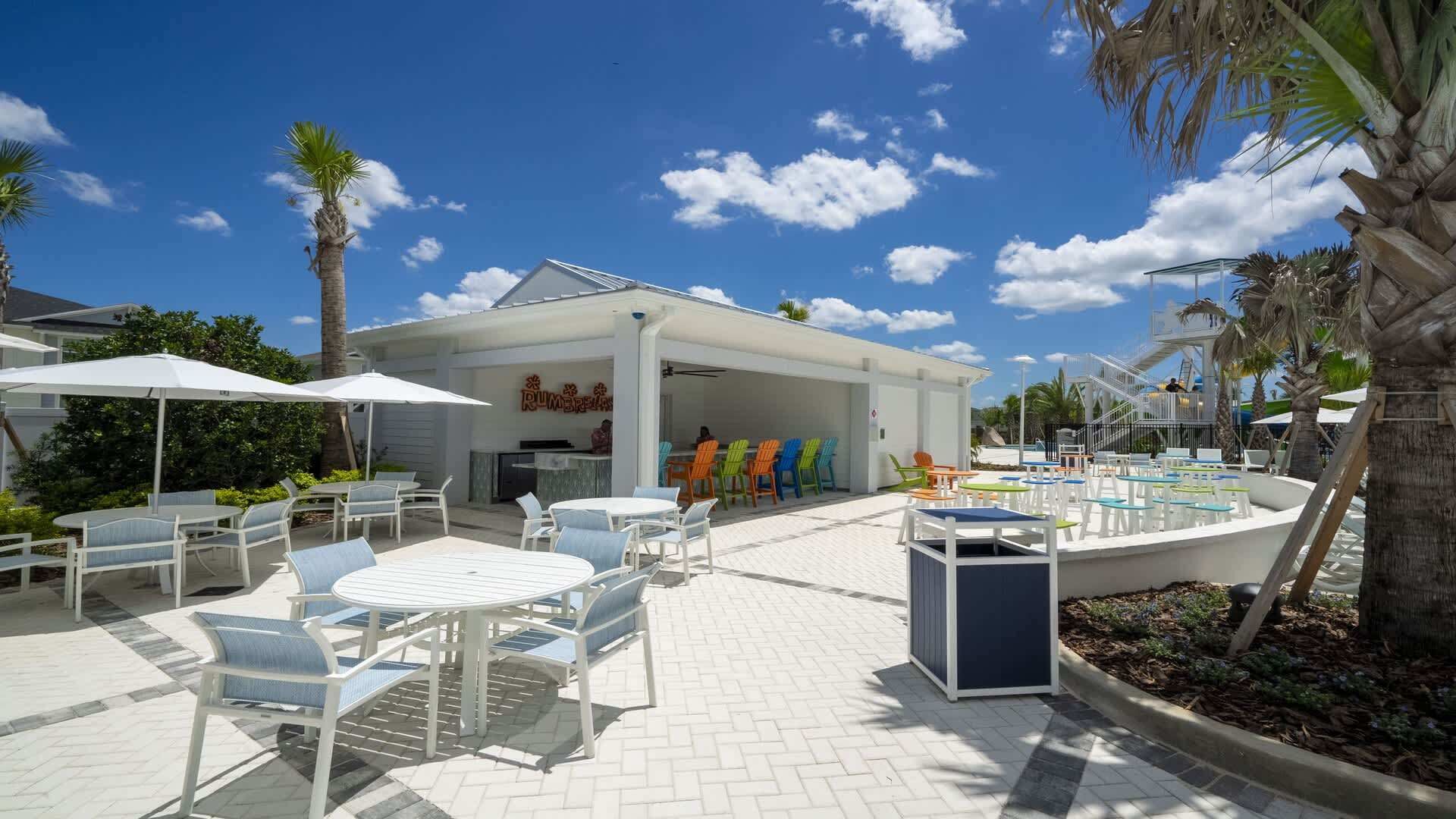 An outdoor patio area with white tables and chairs, a covered seating area, and a pool.