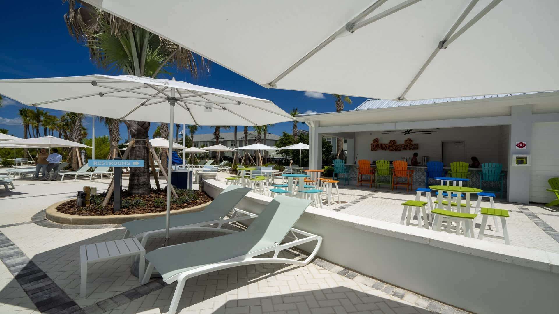 Un espace aménagé au bord de la piscine, avec des chaises longues, des parasols et un restaurant appelé « RUMBRELLAS ».