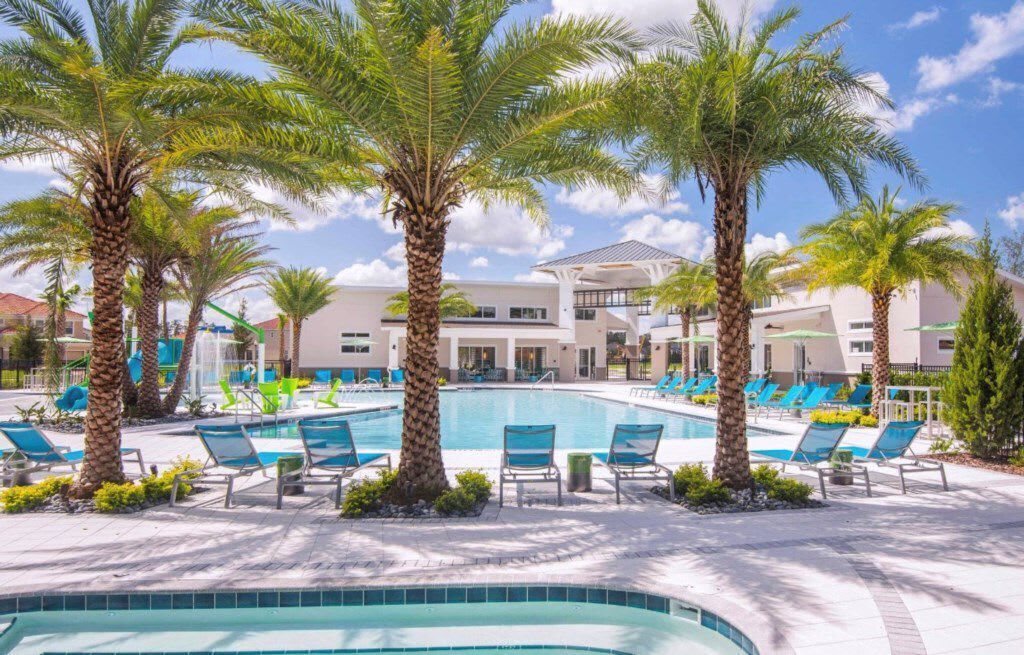 A pool area with palm trees, lounge chairs, and a building in the background.
