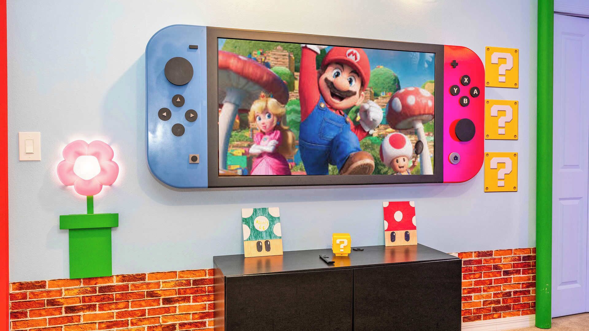 A wall-mounted television displaying a video game scene, a flower-shaped light, and two question mark-shaped decorations.