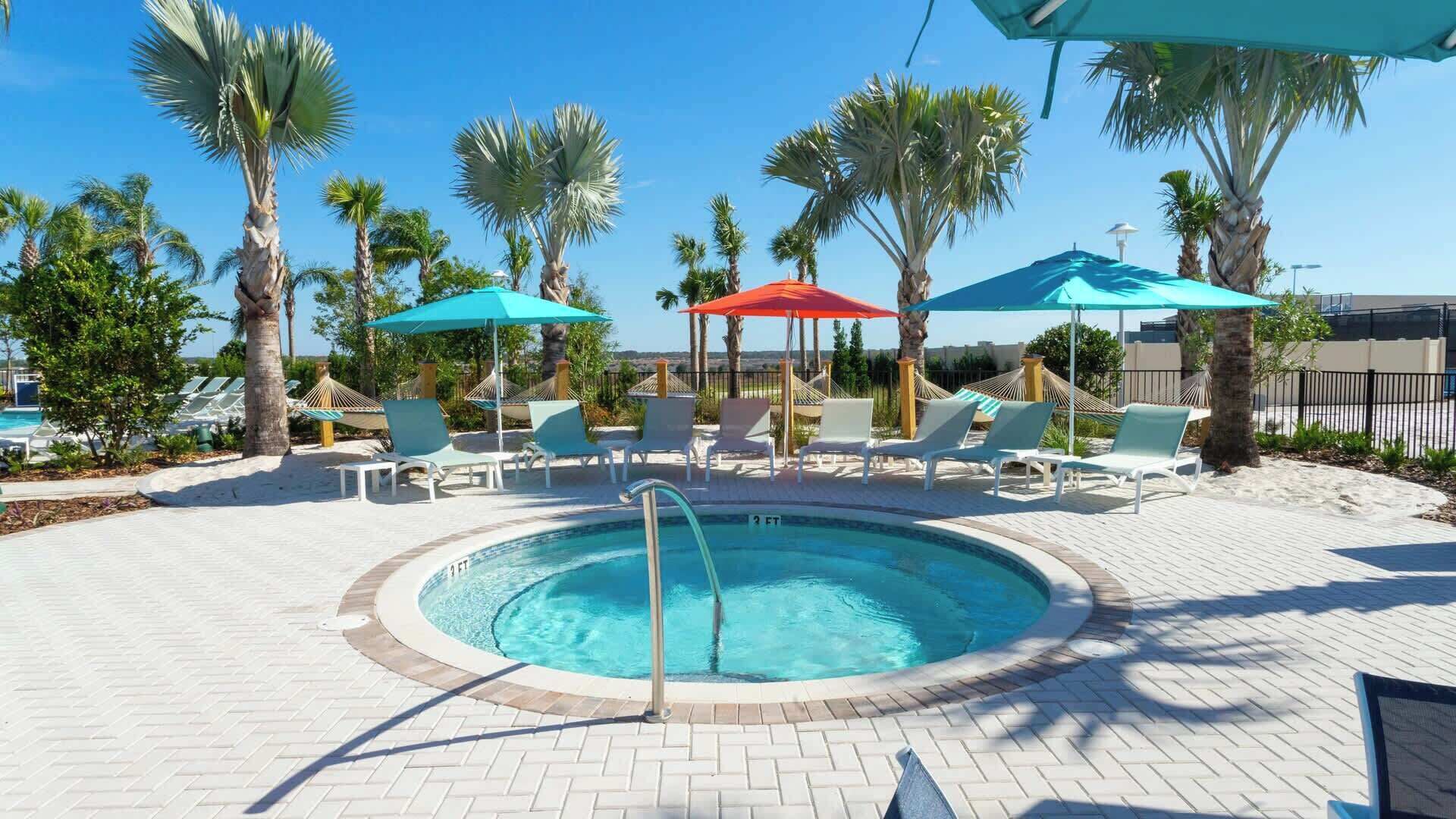 A pool area with lounge chairs, umbrellas, and palm trees.
