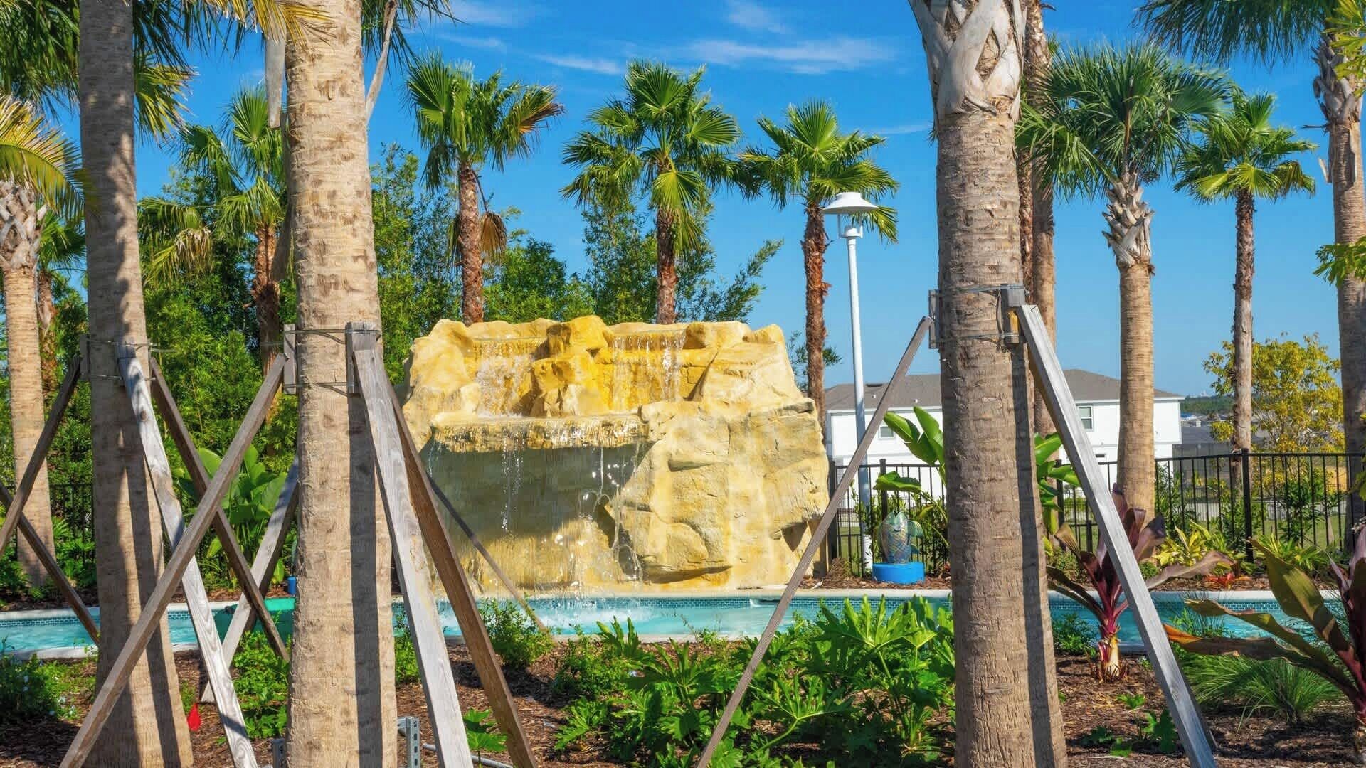 Eine Felsformation mit einem Wasserspiel, umgeben von Palmen und einem Pool.