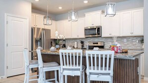 A modern kitchen with white cabinetry, stainless steel appliances, and a central island with seating. - Luxury 5BR House Private Pool & BBQ Sleeps 18 (Davenport)