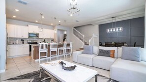 Eine moderne Küche mit weißen Schränken, ein Essbereich mit weißen Stühlen, ein weißes Sofa und eine Treppe.