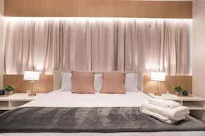Ein Hotelzimmer mit einem großen Bett, zwei Nachttischen mit Lampen, einem Kopfteil und einem Fenster mit Vorhängen.