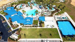 Vista aérea de um resort com piscina central, várias áreas de descanso e quadra de tênis coberta espaçosa.