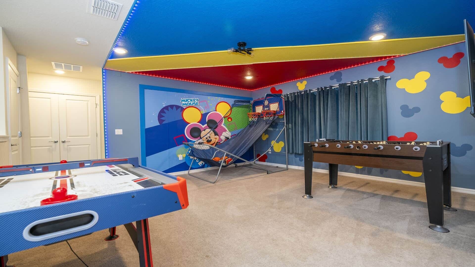 Ein Spielzimmer für Kinder mit einem Tischkicker, einer Rutsche und einer Wandmalerei mit Mickey Mouse.