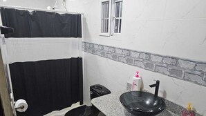 A bathroom with a black toilet, a black sink, a shower curtain, and a window. - Tocumen Comfort Stay (24 de Diciembre)