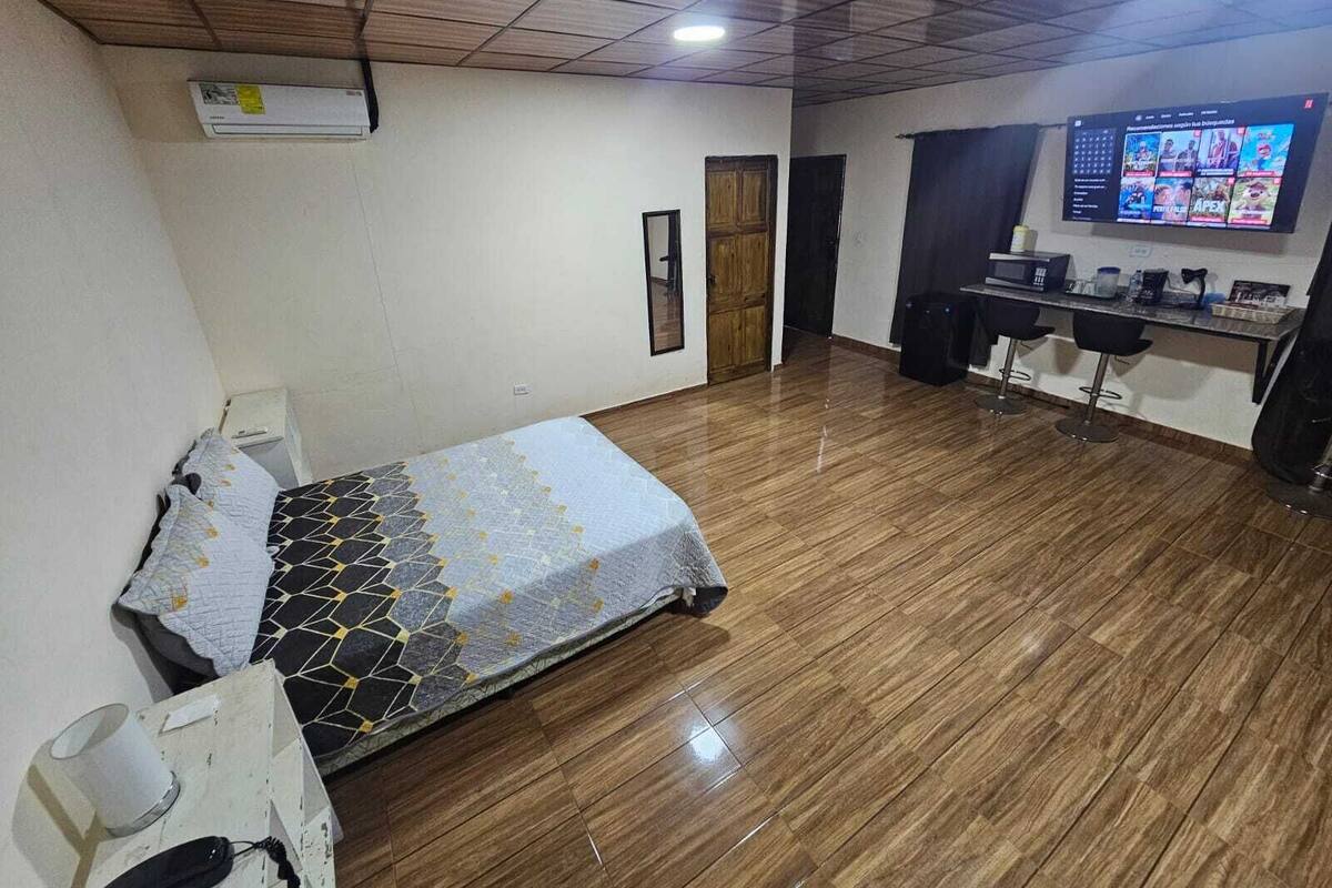 A hotel room with a bed, a desk, a TV, and a kitchenette.