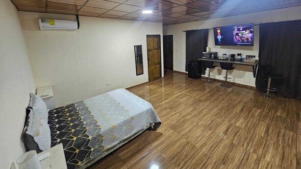 A room with a bed, a desk with a chair, a television, and a door. - Tocumen Comfort Stay (24 de Diciembre)