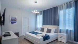 Ein Schlafzimmer mit Bett, Nachttischen, Schreibtisch, Stuhl, Fernseher und einem Bild an der Wand.