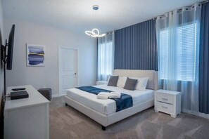 Ein Schlafzimmer mit Bett, Nachttischen, Schreibtisch, Stuhl, Fernseher und einem Bild an der Wand.
