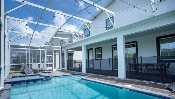 Ein Schwimmbecken mit Glasveranda, Sitzgelegenheiten im Freien und blauem Himmel.