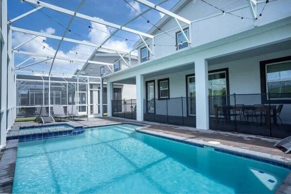 Ein Schwimmbecken mit Glasveranda, Sitzgelegenheiten im Freien und blauem Himmel.