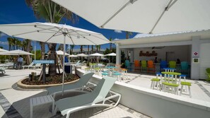 Ein Poolbereich mit Liegestühlen, Sonnenschirmen und einer Bar mit bunten Stühlen.