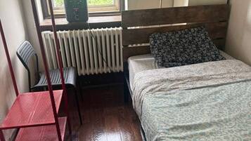 A room with a bed, a chair, a radiator, and a window with blinds.
