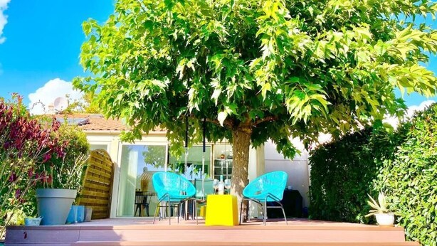 Eine von Bäumen gesäumte Terrasse mit Sitzgelegenheiten und einem Hauseingang.