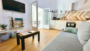 Ein Wohnzimmer mit einer Couch, einem Couchtisch, einem Fernseher, einer Küchenzeile mit Schränken und einer Tür zu einem anderen Raum.