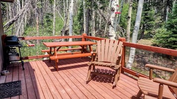A wooden deck with a picnic table and chairs, surrounded by trees.