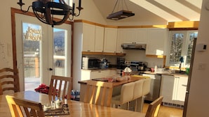 Uma cozinha ampla com armários brancos, uma mesa de jantar de madeira e um lustre.