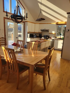 Una cocina amplia con gabinetes de madera, un comedor con una mesa grande y sillas, y una lámpara colgante.
